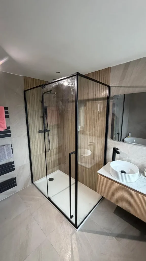 Black-framed walk-in shower enclosure with wood-effect wall panels and fluted vanity unit
