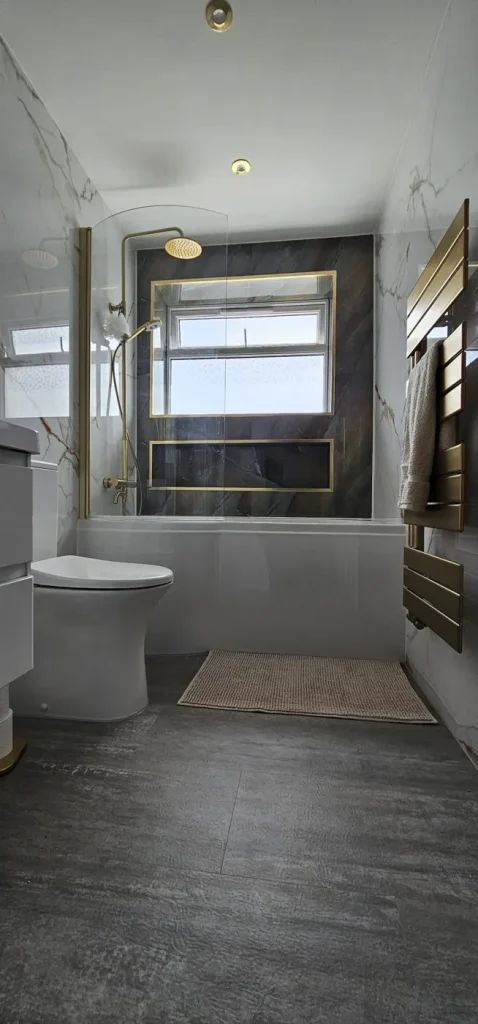 Finished bathroom with marble-effect walls, dark feature wall with brushed-gold framed niches, gold rainfall shower over the bath and gold towel radiator